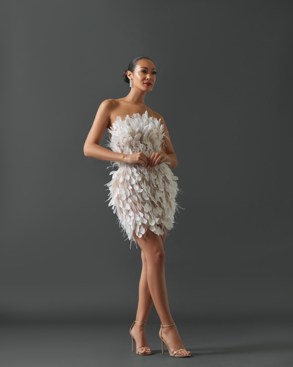 Strapless mini dress featuring feathers and glass beads on entire gown. Embellishment radiating from waist and constructed on a sheer/nude shell.