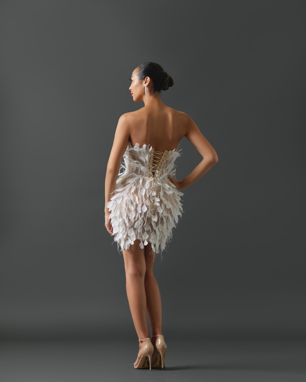 Strapless mini dress featuring feathers and glass beads on entire gown. Embellishment radiating from waist and constructed on a sheer/nude shell.