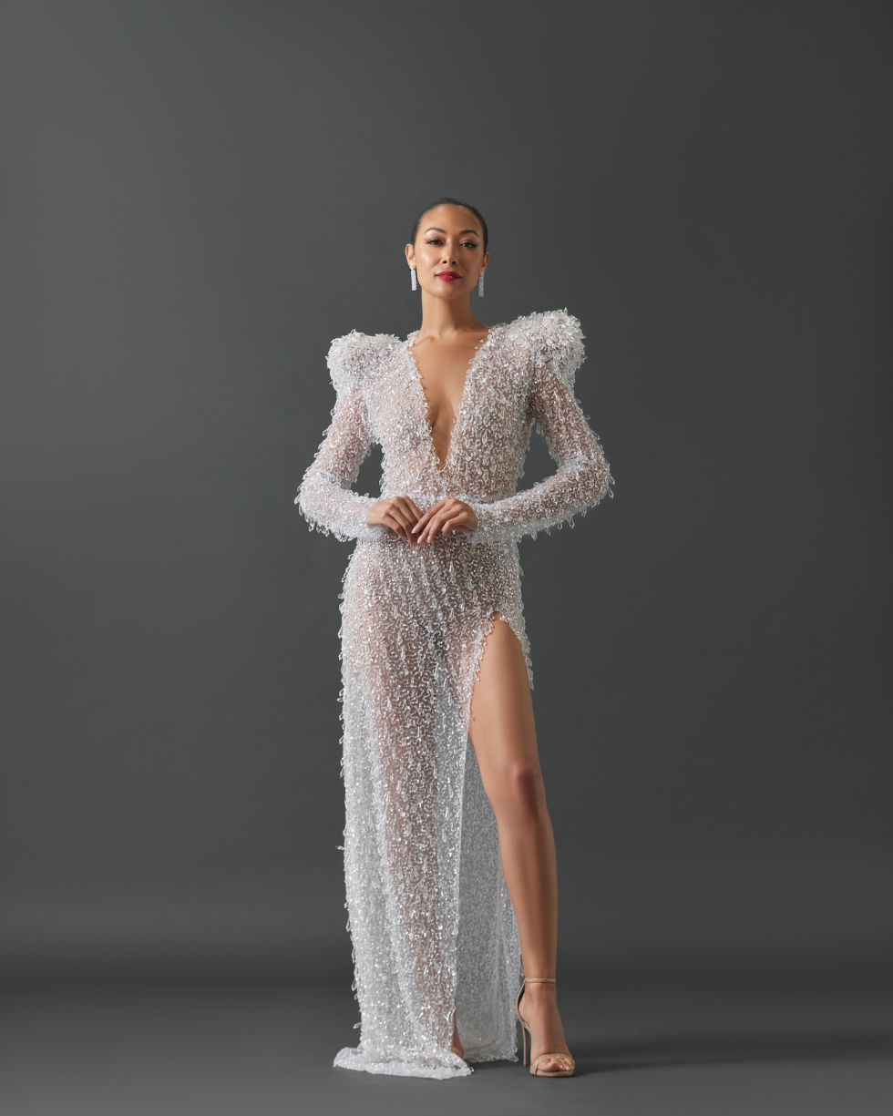 Sheer column gown with a high slit and deep V in neckline. Gown features long sleeves and exaggerated, structured shoulders. Fabrication and embellishment of gown features heavily patterned sequin mesh and covered with large prism shaped, hanging glass beads.