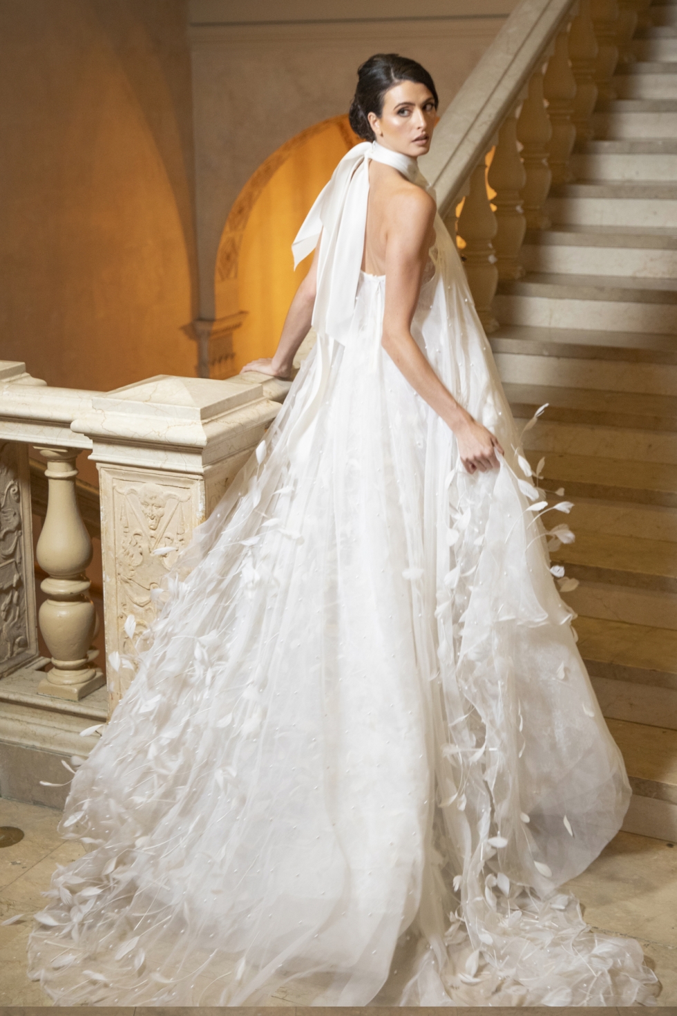 A feather-accented gown with pearl beading, halter neckline, organza bow, and Chantilly lace lining.