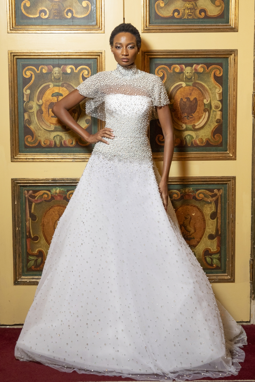 A Moonstone hand-embroidered gown featuring intricate beadwork and a high-neck topper. The gown exudes elegance with its shimmering details, flowing silhouette, and sheer cape- like topper, creating a look of ethereal sophistication.